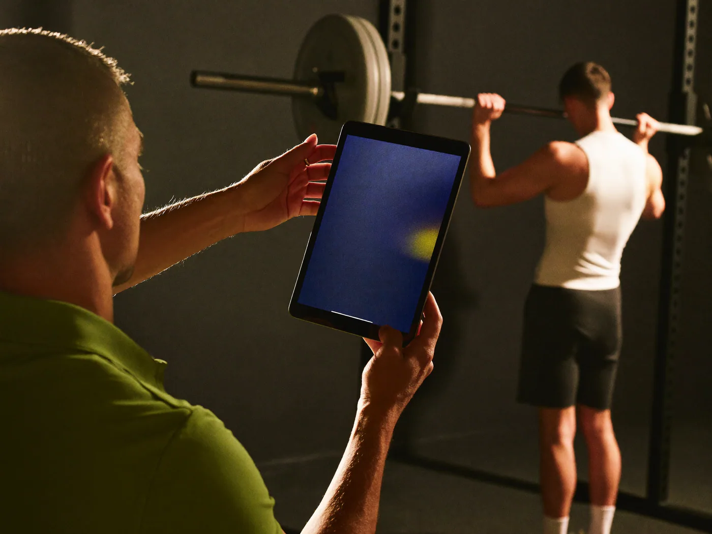 Coach con il tablet accanto a un cliente al rack, durante una sessione in sala