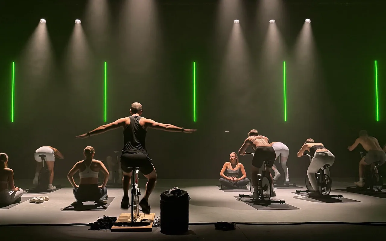 Corso di gruppo in una sala scura di un centro fitness, con l’istruttore sul palco