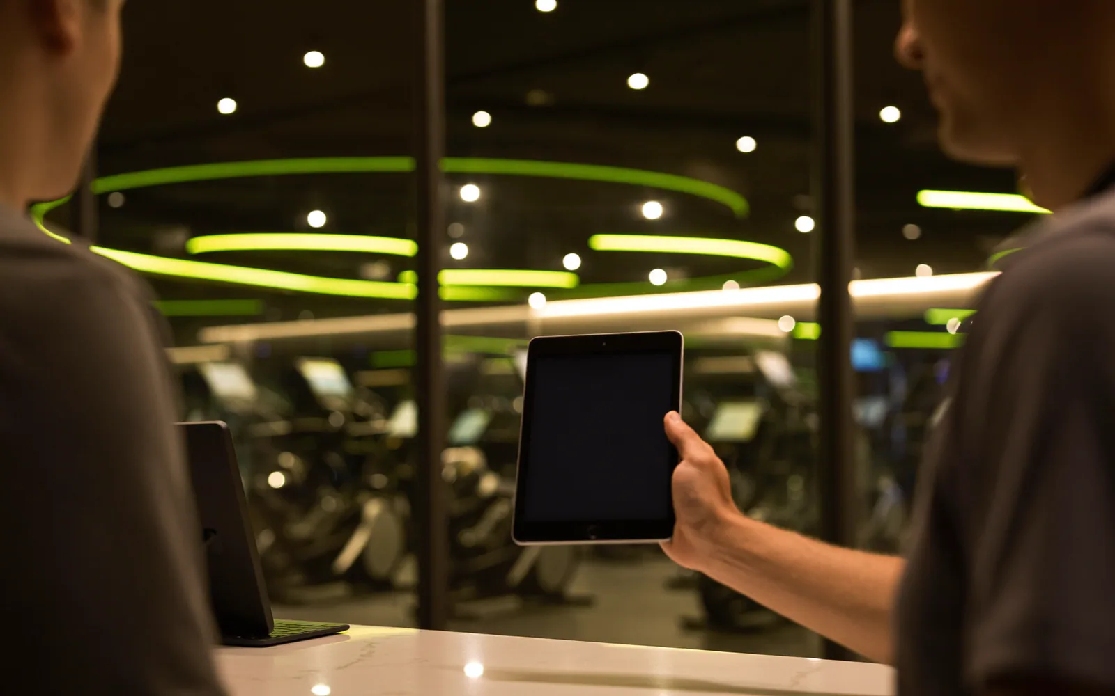 Reception di un centro fitness con un tablet sul bancone e la sala pesi sullo sfondo